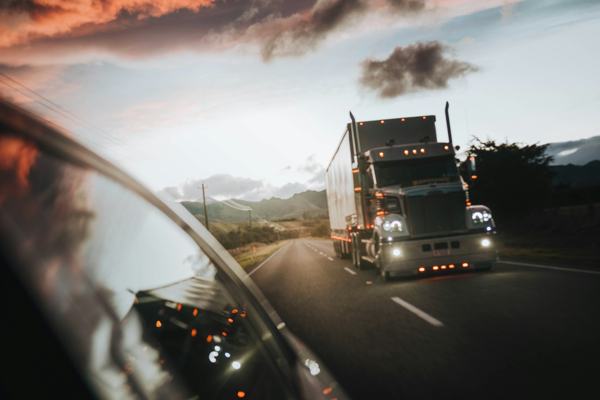 Semi truck with headlights on, driving a highway at dusk